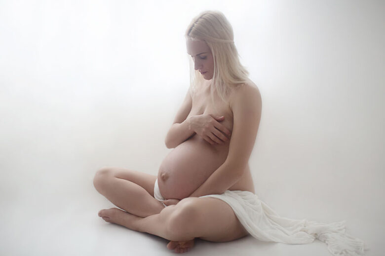 Maternity Photography London | backlit semi nude portrait of a pregnant woman covered with a white drape material