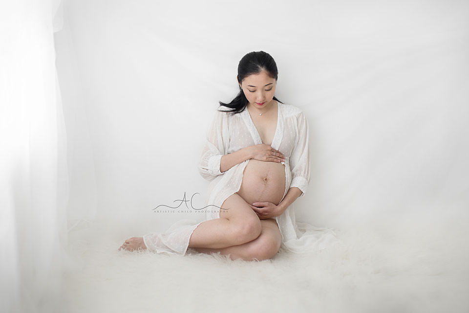 South East London Pregnancy Photographer | Phoebe 7 maternity portrait of pregnant woman sitting on the floor and embracing  her bump | London