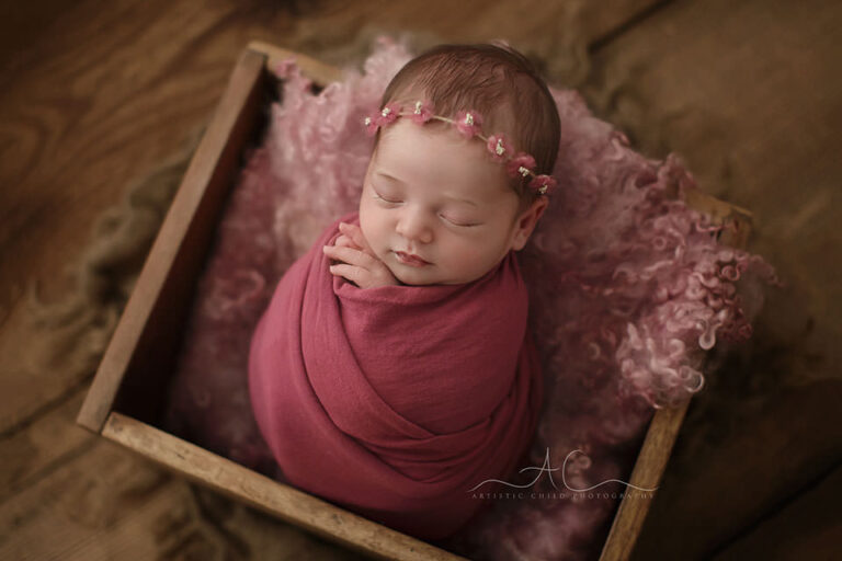 London Newborn Baby Girl Photos | newborn baby girl swaddled in the pink wrap sleeps in a wooden crate