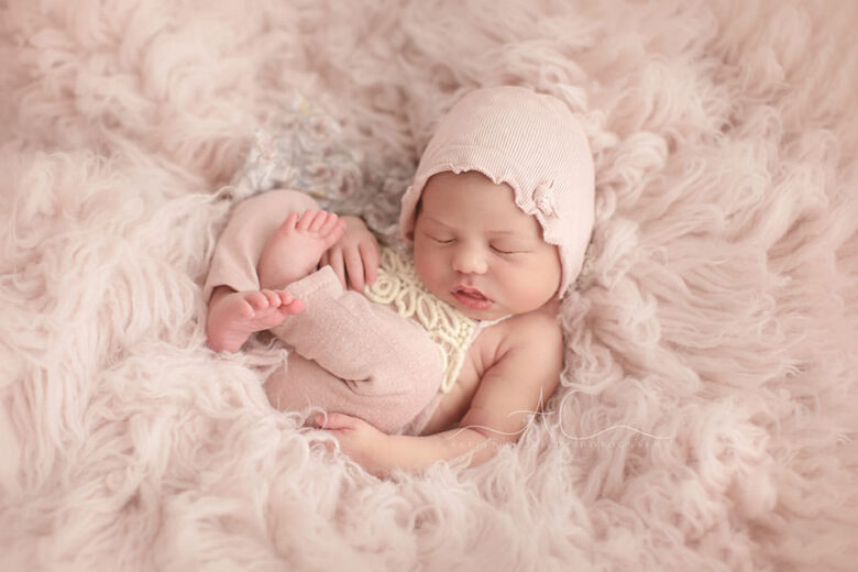 Professional Bromley Newborn Photography Services | newborn baby girl wears pink romper and a hat while photographed during her newborn photo session