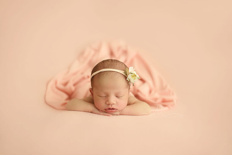 Bromley Newborn Baby Girl Photos | portrait of a newborn baby girl with a flower hairband sleeping in hands under chin position