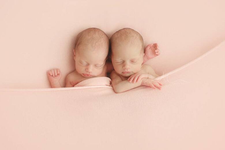 Bromley Newborn Twin Girls Photos | portrait of twin girls hugging each other covered by a pink blanket