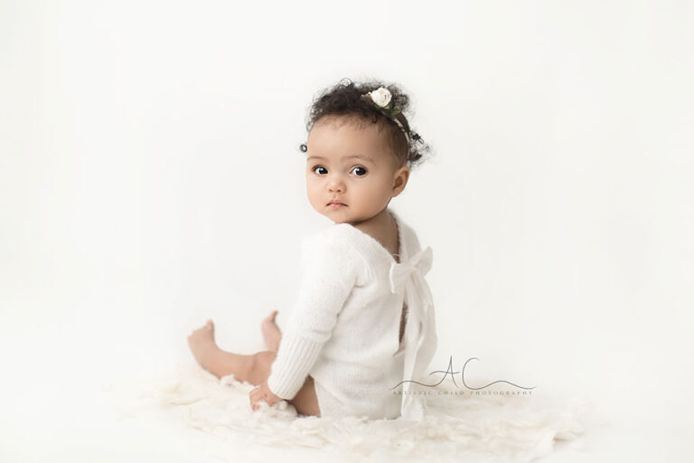 London Baby Girl Pictures | Elena 2 London Baby Girl Pictures | photo of 7 months old baby girl in a white cashmire romper with a bow at the back