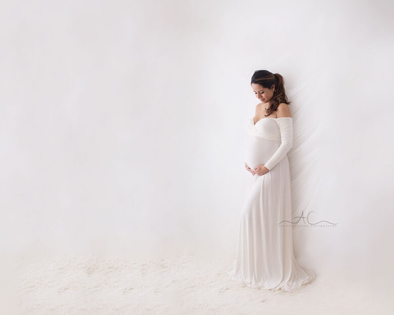 Best London Maternity Portraits | pregnant woman photographed in white dress while looking at her bump
