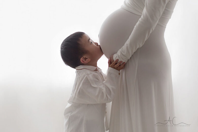 South East London Maternity Photography | 3 year old kisses a bump of her pregnant mother during a professional maternity session