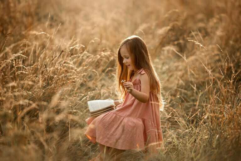 South East London Kids Photos | Aurora 11 South East London Kids Photos | beautifully backlit portrait of a 5 year old girl reading a book in the middle of a long grass field