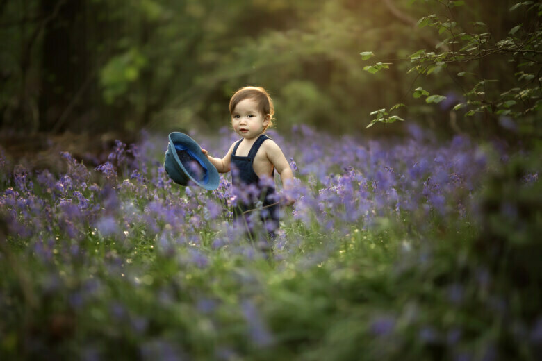 Dreamy Bluebells London Children Photography | portrait of 18 months old boy taking off his hat in the middle of bluebells patch