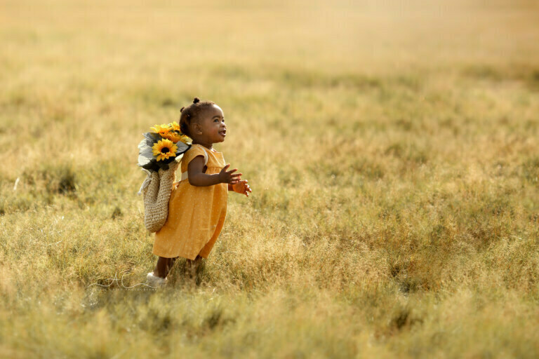 Beautiful London Toddler Photography | happy 1 year old girl runs through the meadow with sunflowers on her back