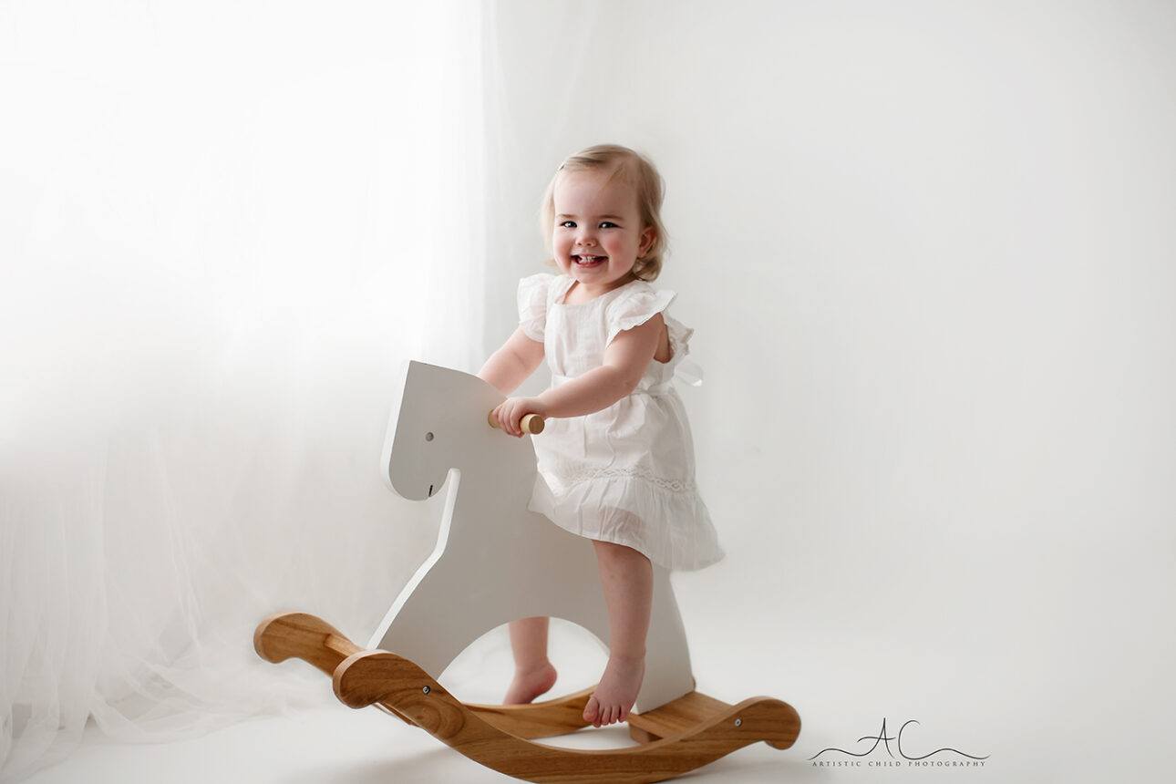 Amazing South East London Toddler Images | smiley portrait of a toddler girl enjoying her ride on a rocking horse during a professional photo session 