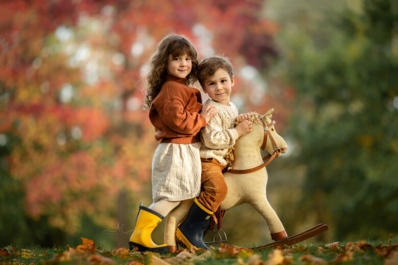 Wonderful London Autumn Sibling Photo Session | portrait of a boy and a girl sitting on a rocking horse in the park during autumnal photoshoot