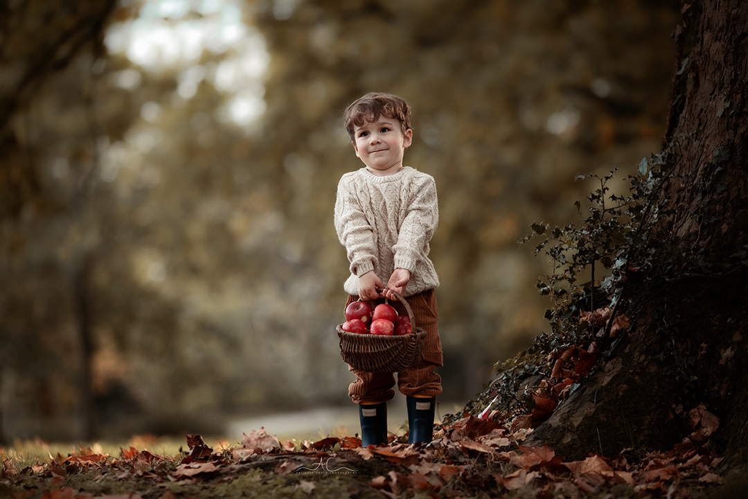 Stunning London Sibling Photo Session | Aurora & Dominic 5 2 year old boy curries a wicker basket full of red apples in a local London park