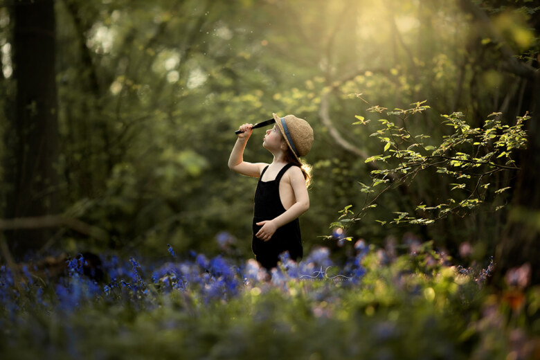 Magical Bluebells Mini Sessions London | portrait of a boy standing in the park full of bluebells and looking through a magnifying glass