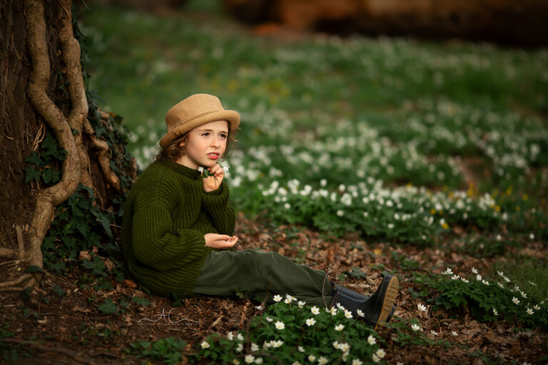 Best London Spring Child Photos | an 8 year old boy sitting under an old tree in the park and holding a bunch of white spring flowers