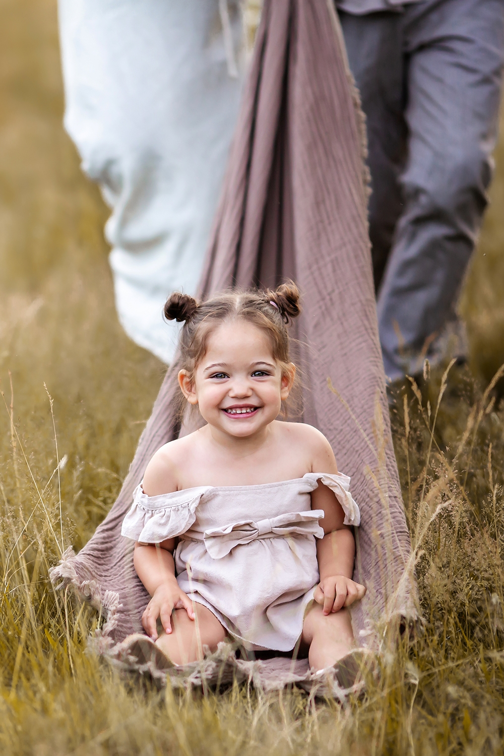London Summer Family Minis | portrait of a 2 year old girl smiling while parents pull her on the blanket through the grass field