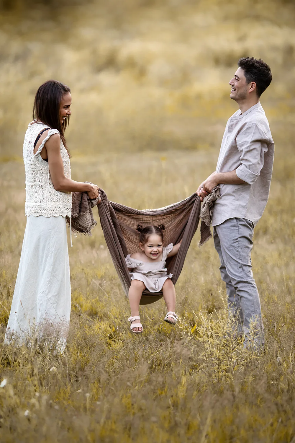 London Summer Family Minis | parents swing her 2 year old daughter in the blanket during a family photoshoot