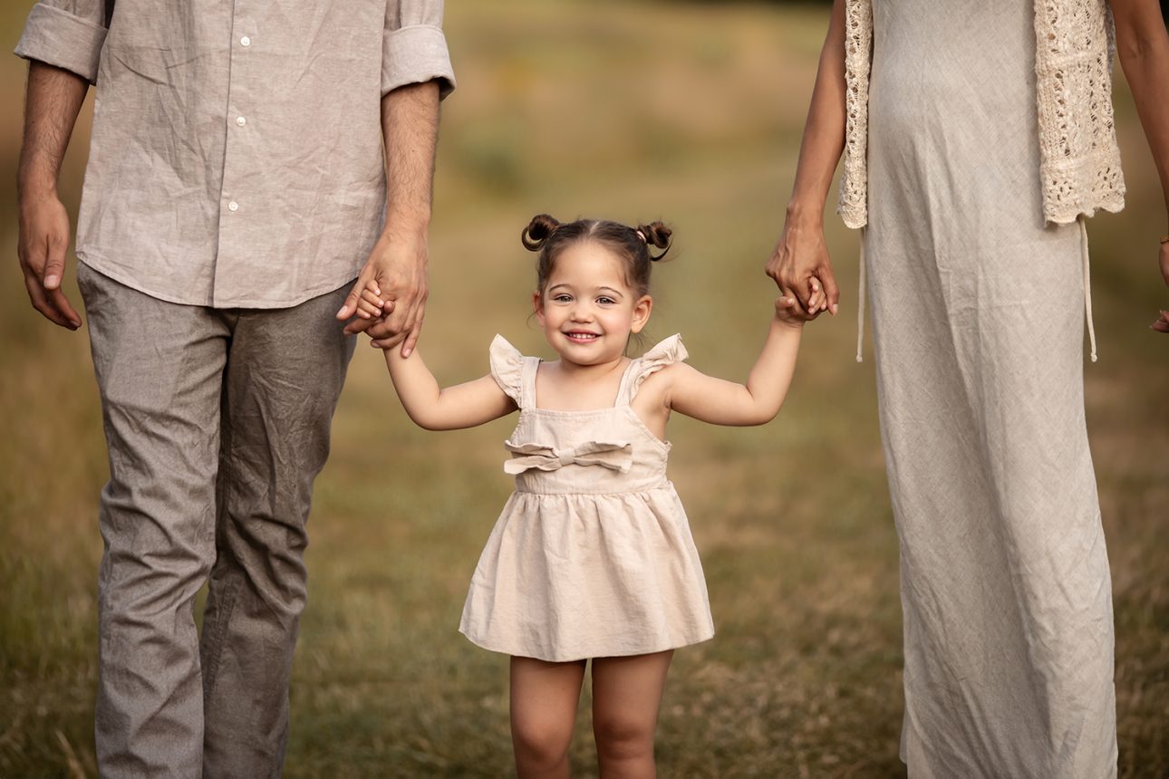 London Summer Mini Sessions | a close up portrait of a 2 year old girl holing Mum's and Dad's hands