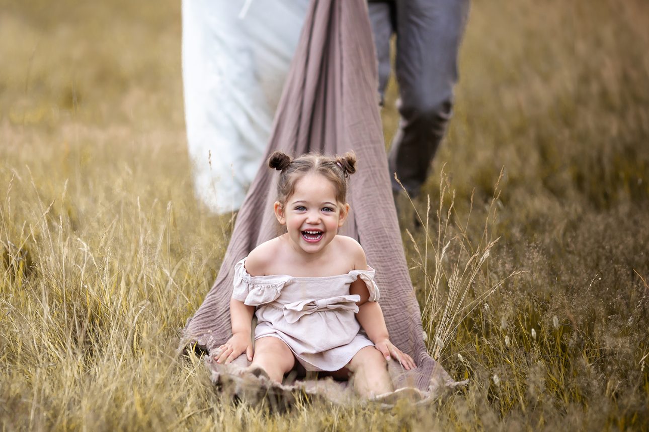 London Summer Mini Sessions | portrait of a 2 year old girl laughing while enjoying a slide ride in the park