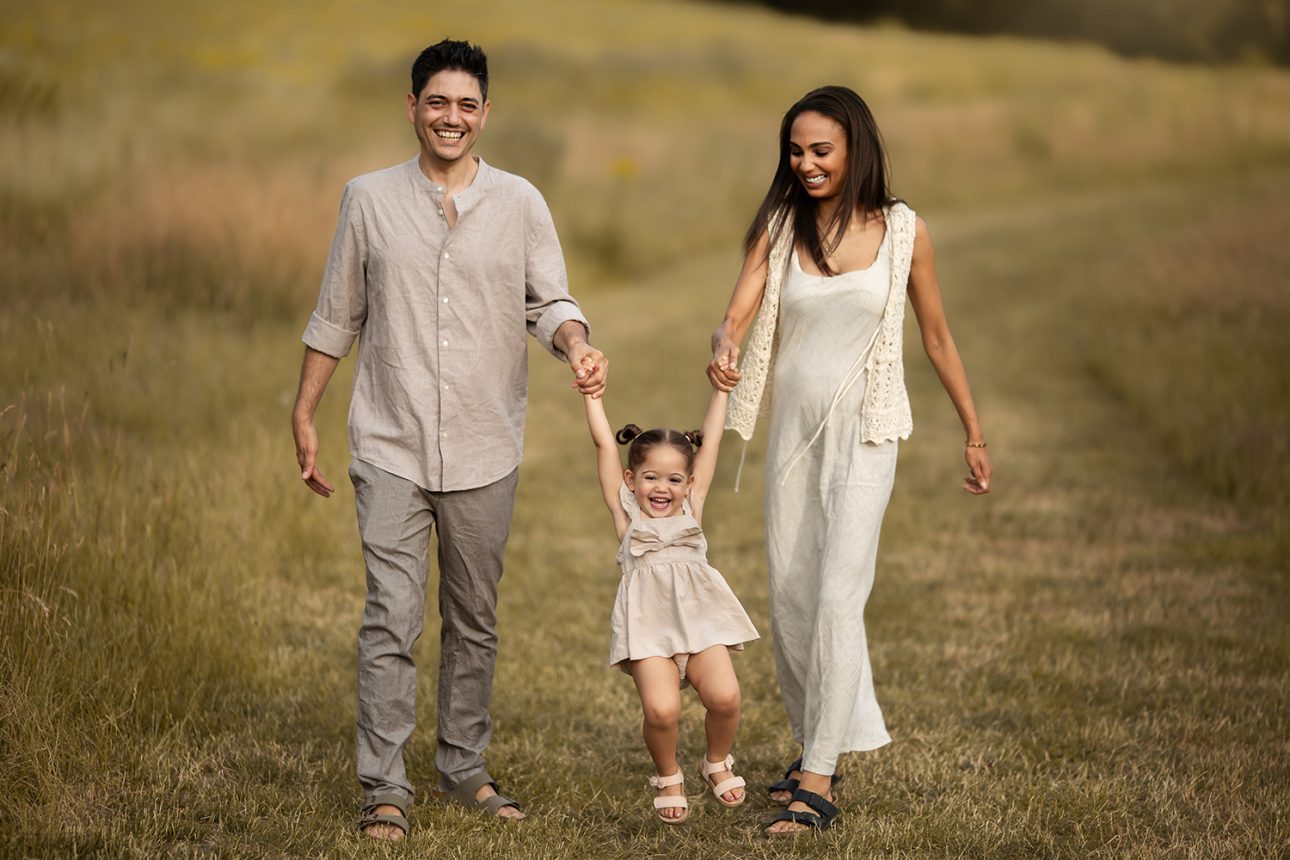 London Summer Mini Sessions | parents swinging her 2 year old daughter while walking through the grass field during a family photoshoot