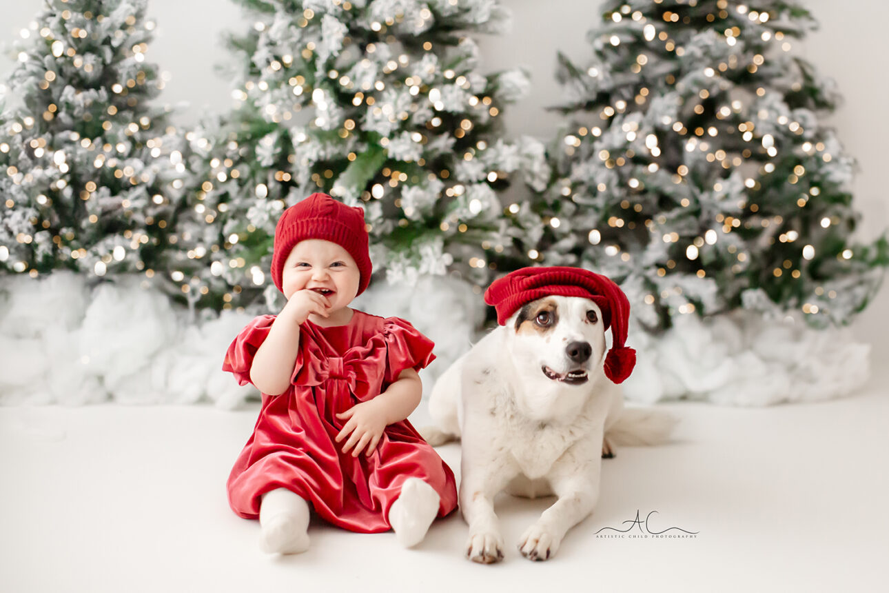 London Christmas Mini Sessions | baby girl and her dog wearing Santa hats during their Christmas photoshoot.