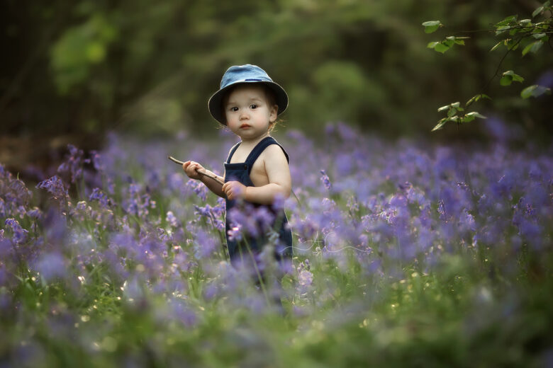 Beautiful Bluebells Mini Sessions London 2025 | portrait of a 1 year old toddler playing with the stick while enjoying bluebells flowers